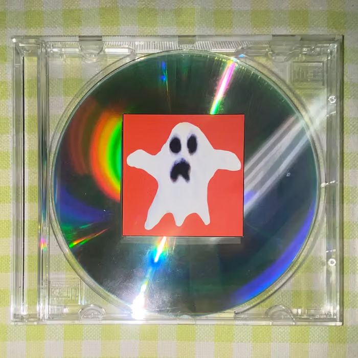 Fotografia d'una funda de CD amb un CD dins i una enganxida amb el dibuix d'un fantasma que cobreix parcialment el CD.